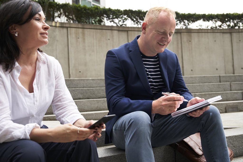 woman-and-man-having-a-discussion-while-sitting-on-steps-2977567 A man and woman engage in a work-related discussion outdoors in London.