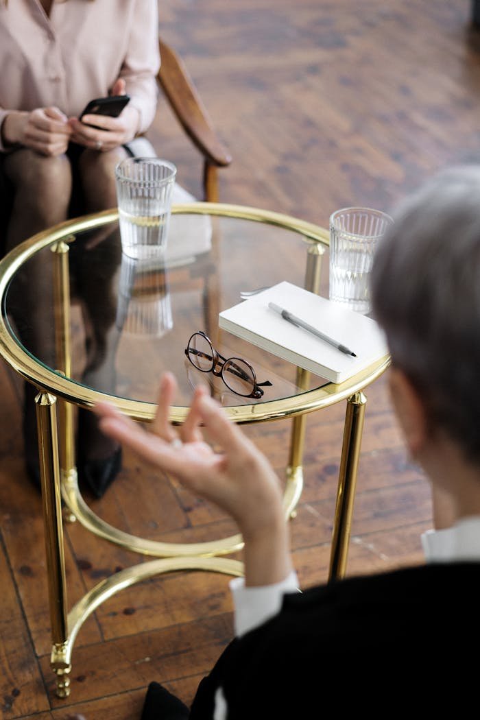 about-us Two adults engaged in a therapy session, seated at a glass table with notebooks and water glasses.